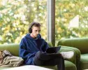 un étudiant assis dans un canapé vert avec un casque et un ordinateur