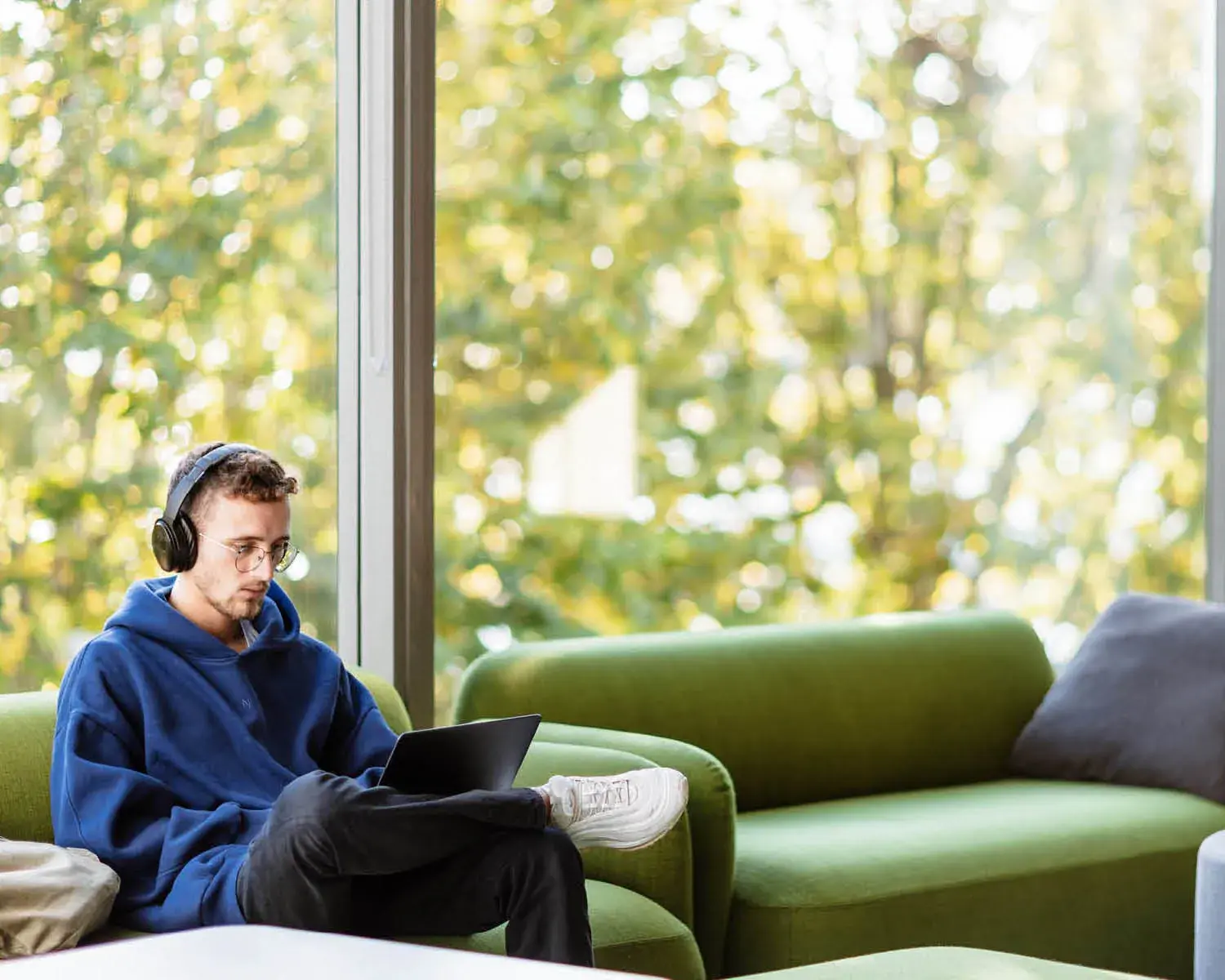 un étudiant assis dans un canapé vert avec un casque et un ordinateur