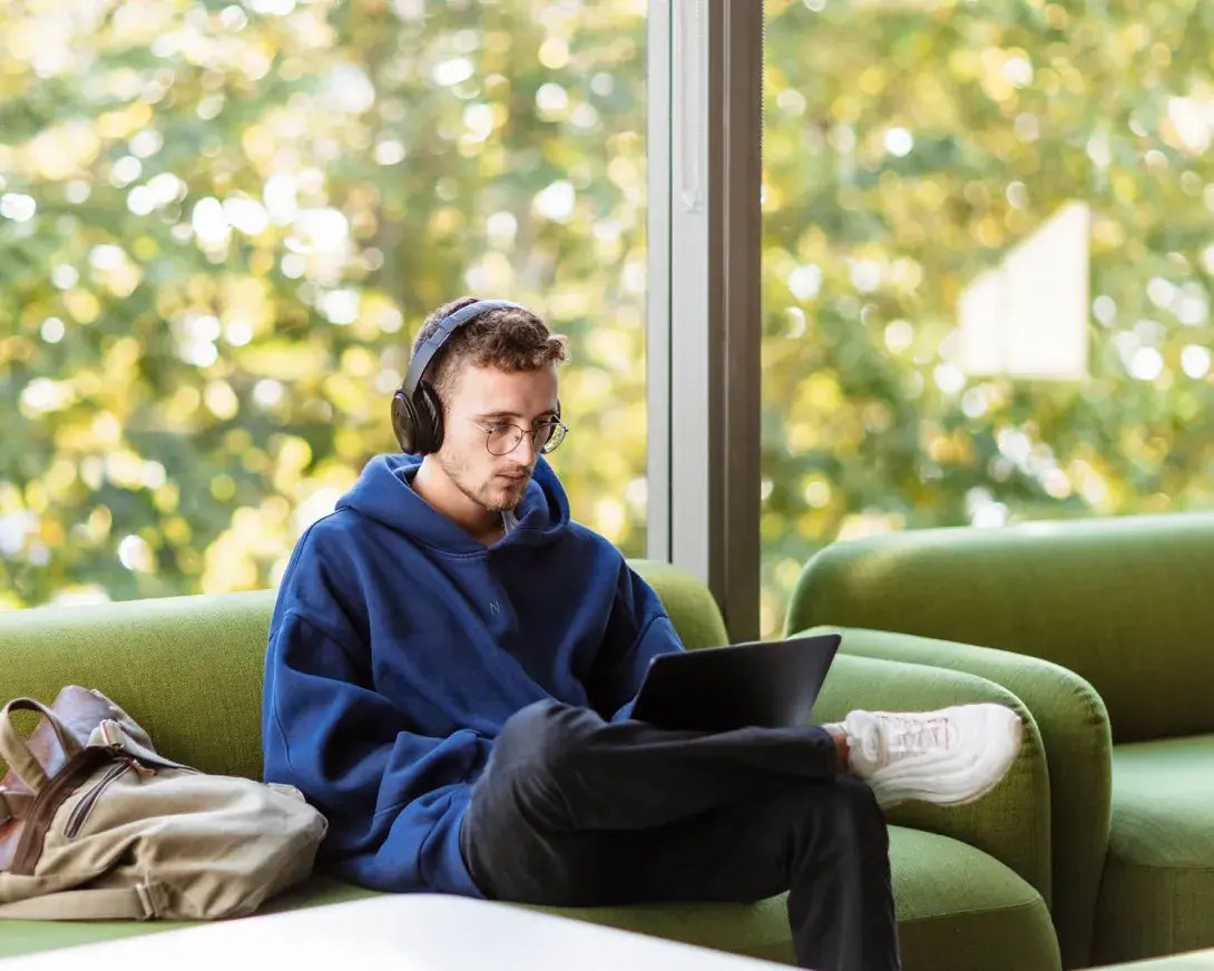 un étudiant assis dans un canapé vert avec un casque et un ordinateur